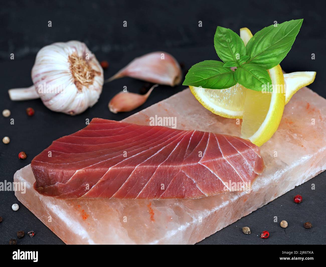 steak de thon cru sur pierre salée avec basilic, citron et ail sur fond d'ardoise noire Banque D'Images