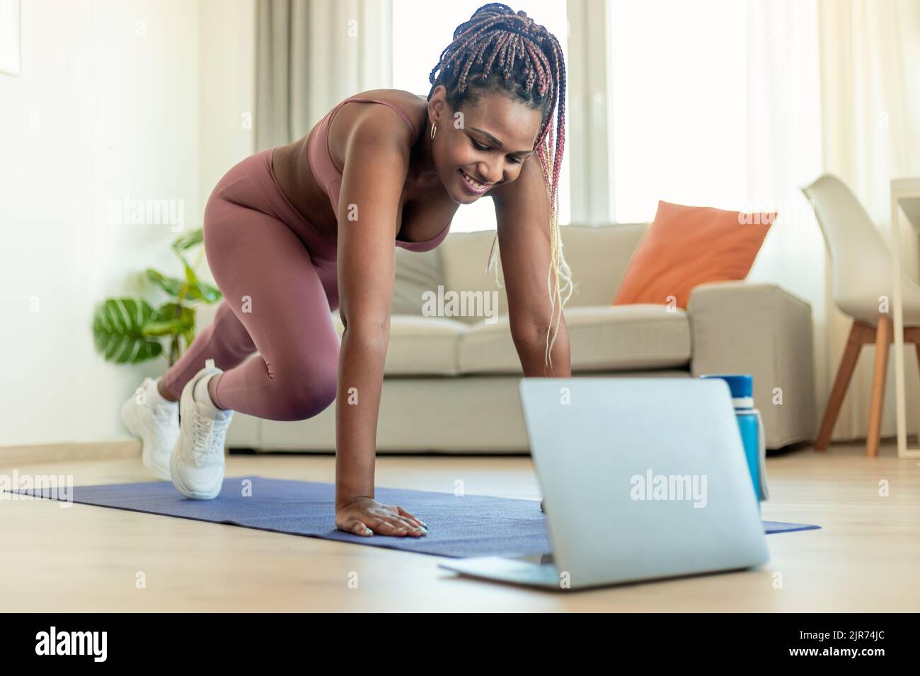 Formation à domicile. FIT noire dame faisant le cross corps alpinistes exercice, regardant le tutoriel en ligne sur ordinateur portable Banque D'Images