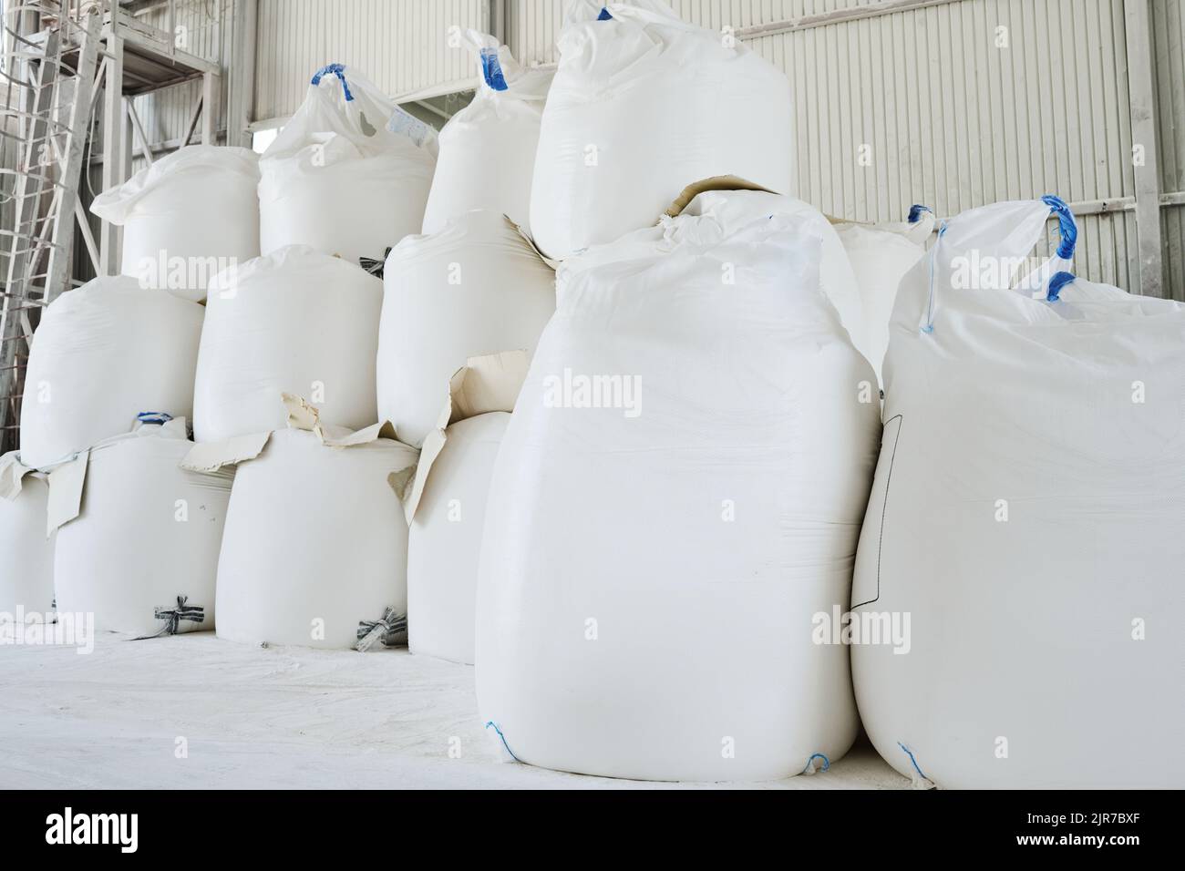 Des tas d'énormes sacs blancs contenant des matières premières en vrac préparés pour le processus de production dans un entrepôt ou une salle de stockage spacieux Banque D'Images