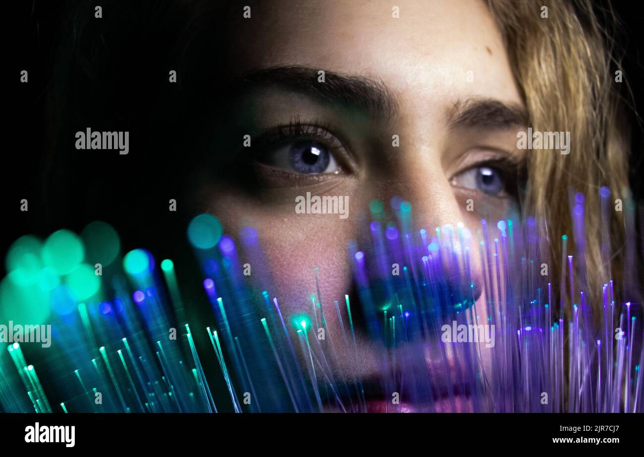 La femme regarde à travers le bokeh futuriste de couleur sarcelle, femme millénaire avec technologie avancée de fibre optique, Noël Banque D'Images