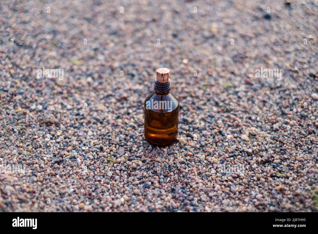 Bouteille d'huile essentielle sur une plage avec des rochers. Petite bouteille de médecine brune en fond de nature. Huile de chanvre biologique CBD. Banque D'Images