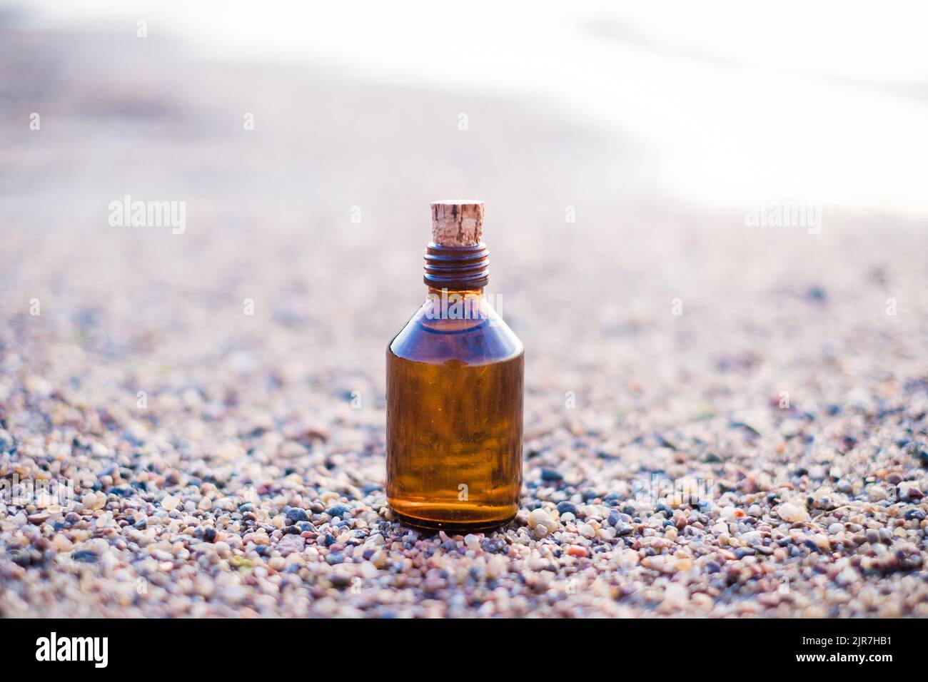 Bouteille d'huile essentielle sur une plage avec des rochers. Petite bouteille de médecine brune en fond de nature. Huile de chanvre biologique CBD. Banque D'Images
