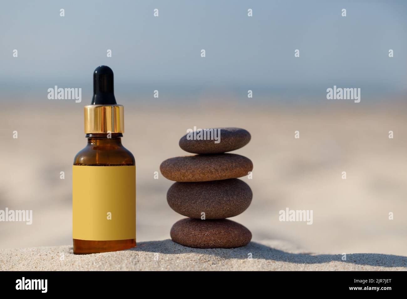 Maquette pour un produit naturel médicinal. Pierres Zen et bouteille d'ambre compte-gouttes sur le sable d'une plage. Copier l'espace. Banque D'Images