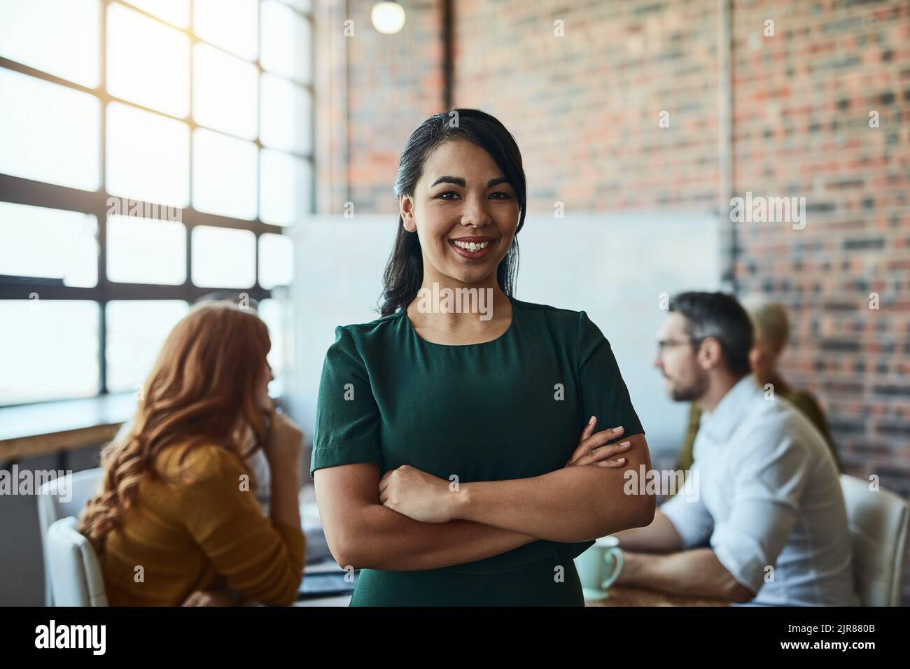 Nous sommes des penseurs novateurs. Une femme d'affaires debout dans le bureau avec ses bras repliés en regardant confiant et souriant à la caméra. Banque D'Images