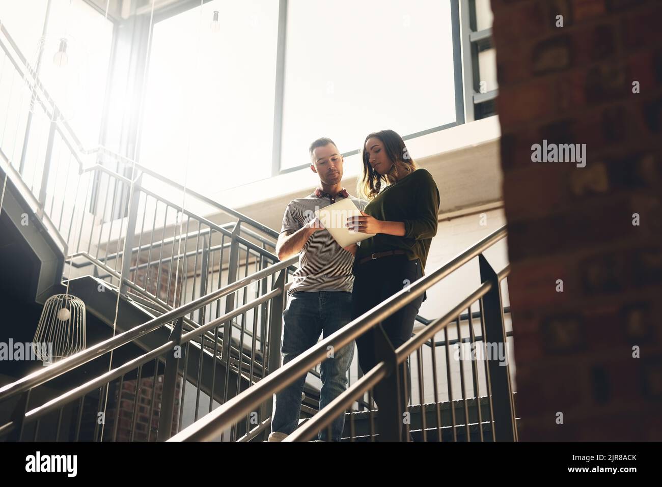 Marchez avec moi... photo sous angle de deux jeunes designers regardant une tablette numérique tout en marchant dans un escalier. Banque D'Images