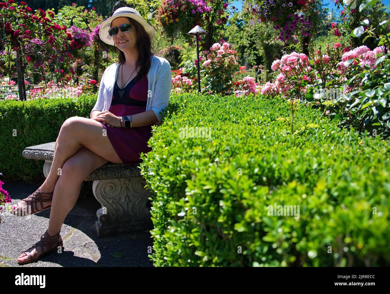 Femme mûre avec chapeau assis sur un banc dans le jardin Banque D'Images