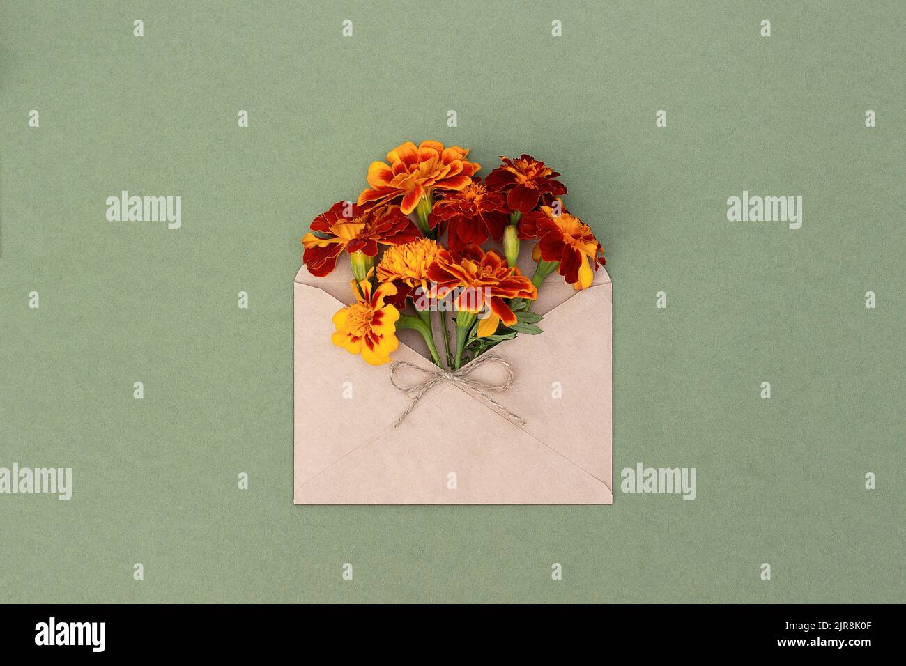 Fleurs orange dans une enveloppe artisanale sur fond vert. Vue de dessus Flat lay. Carte de vœux minimale pour l'été ou l'automne. Banque D'Images