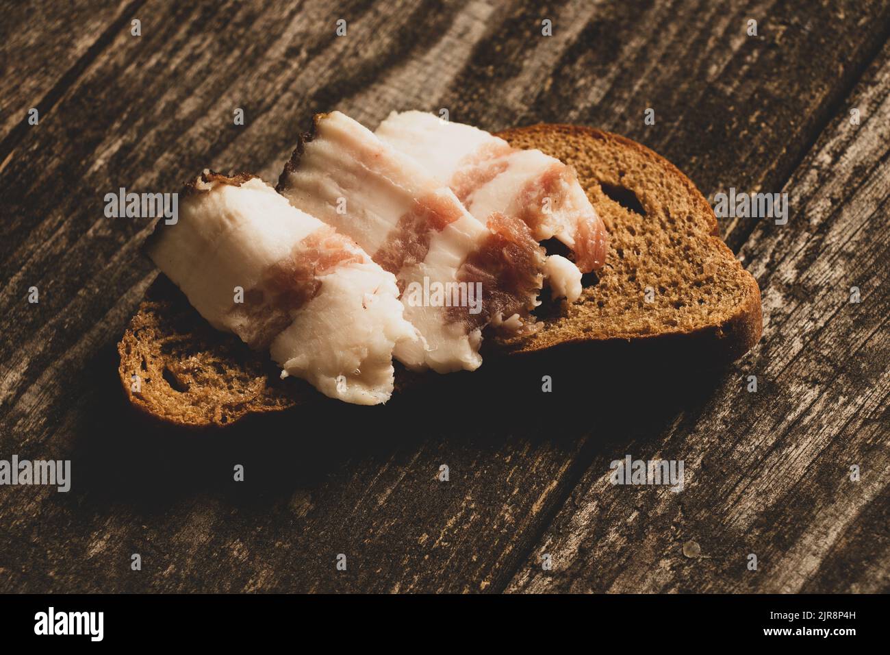 un morceau de pain noir et de tranches de bacon se trouve sur une table en bois, du pain au bacon Banque D'Images un morceau de pain noir et de tranches de bacon se trouve sur une table en bois, du pain au bacon Banque D'Images