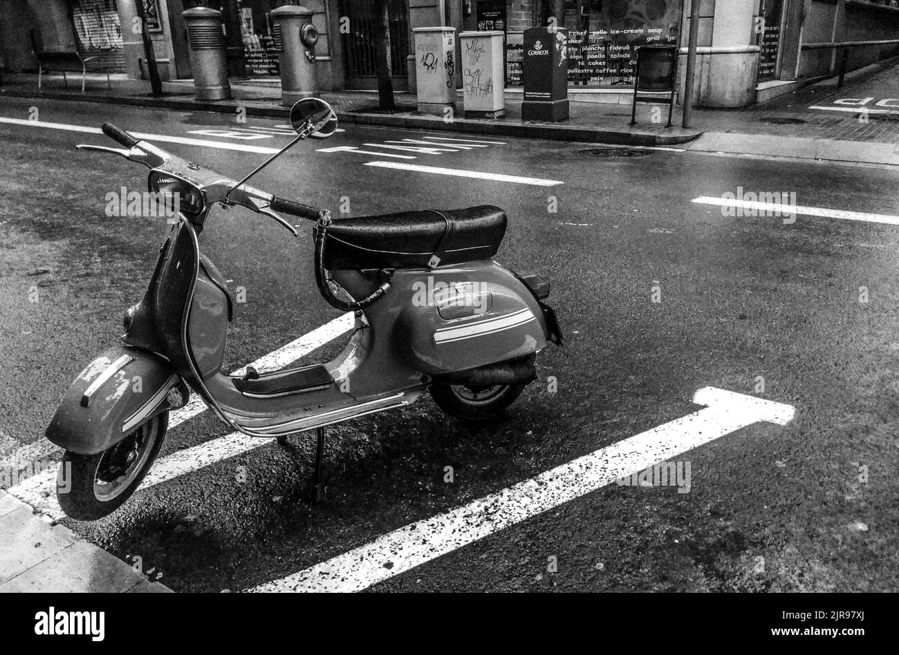 Une photo en niveaux de gris d'un scooter Vespa italien stationné sur la route Banque D'Images