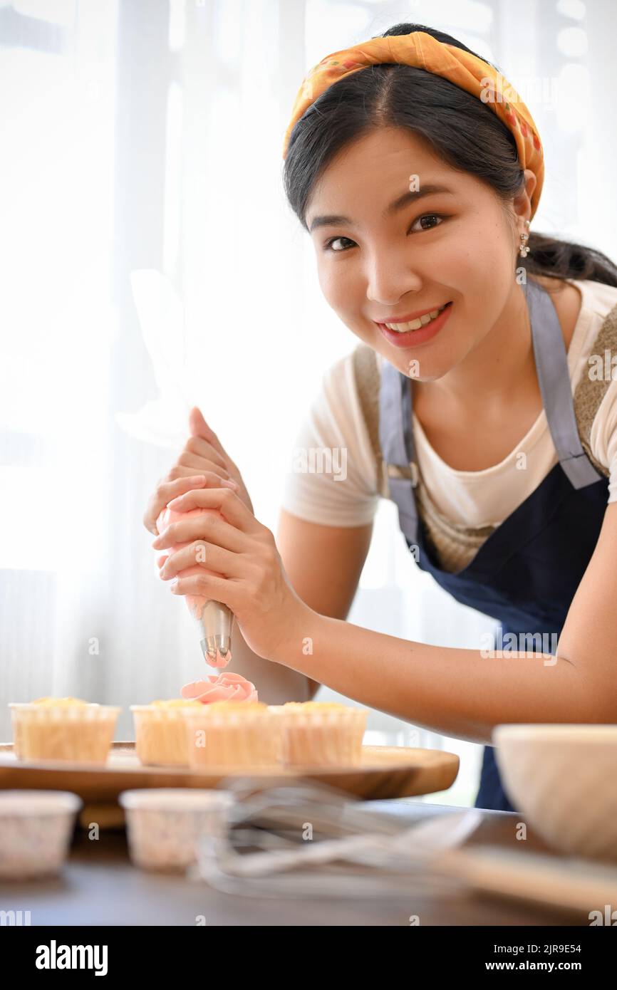 Belle femme faisant le cupcake, décorant le cupcake avec la crème dans la cuisine Banque D'Images