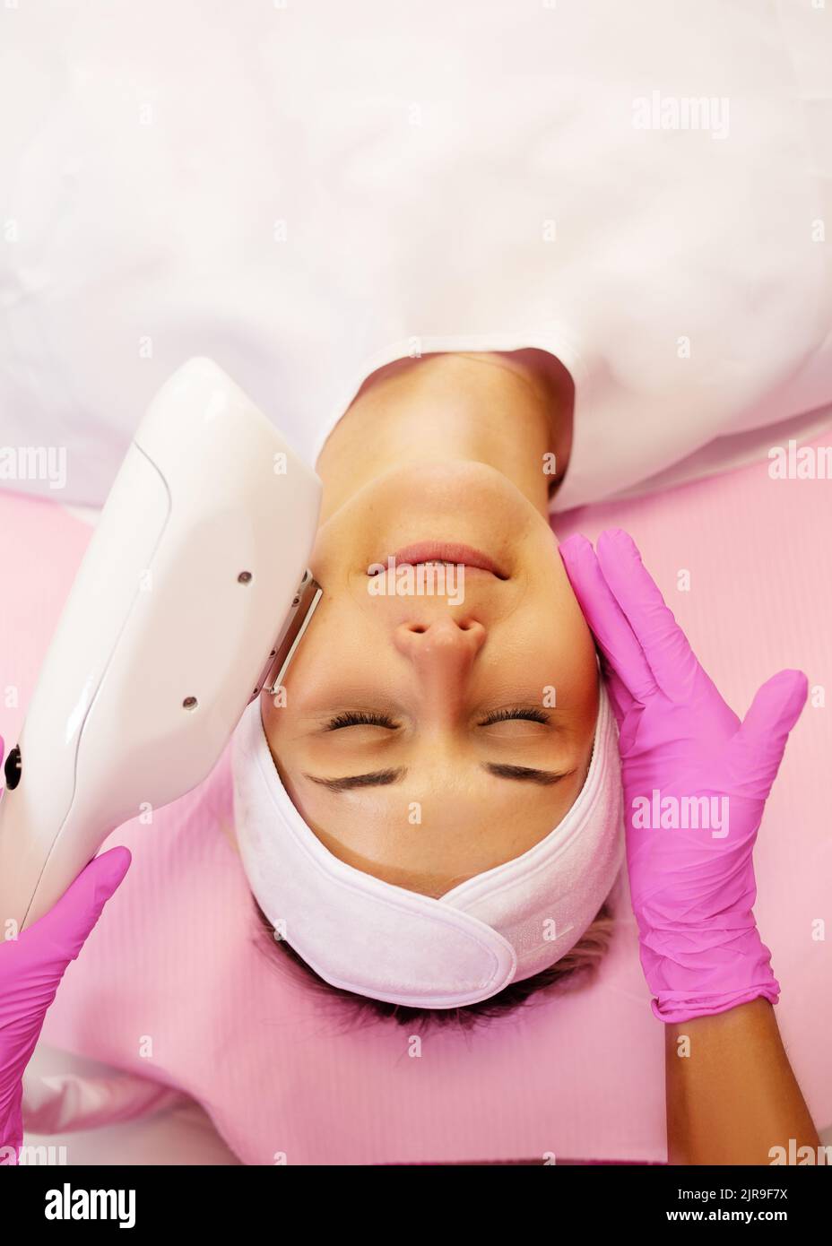 Vue de dessus de la jeune femme couché avec les yeux fermés, obtenant un traitement de rajeunissement par appareil de beauté laser machine dispositif. Banque D'Images