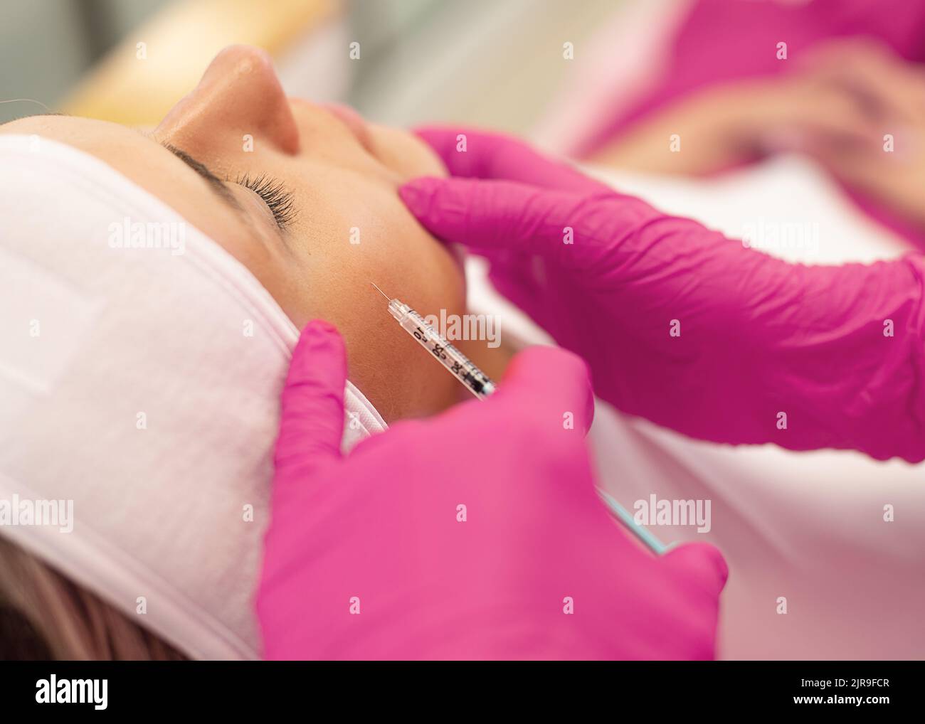 Vue latérale de la jeune femme obtenant rajeunissement injection de collagène dans les pommettes soulevant la peau du visage. Cosmétologie. Banque D'Images