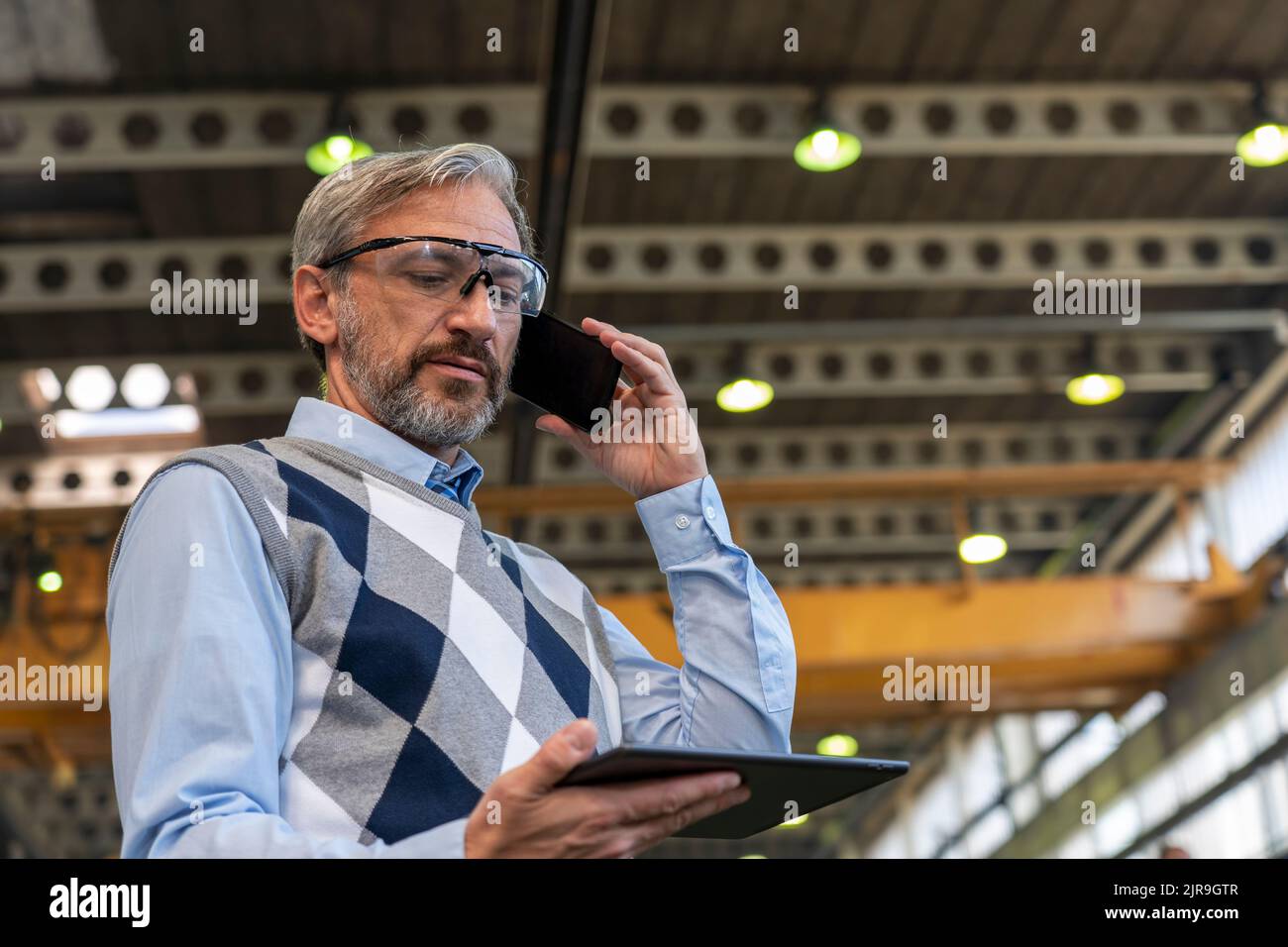 Portrait d'un PDG ou d'un homme d'affaires confiant, élégant et aux cheveux gris. Homme debout et utilisant un smartphone et une tablette numérique. Banque D'Images