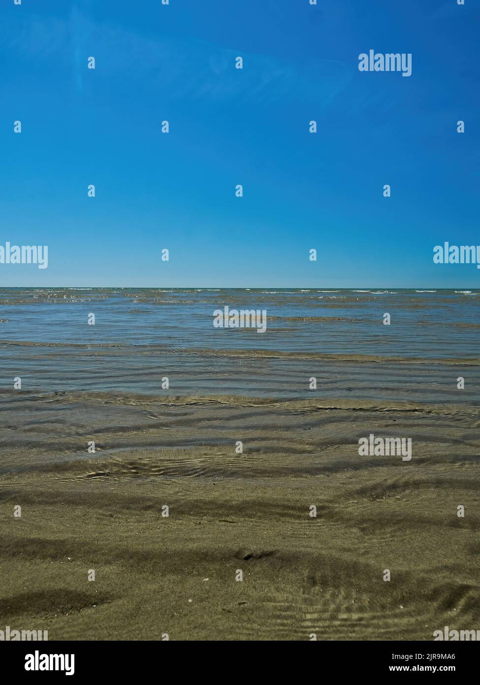 Une vue simple et minimaliste en petit angle sur les vagues douces des échalotes, sur le sable ondulé jusqu'à un horizon et un ciel bleu profond. Banque D'Images