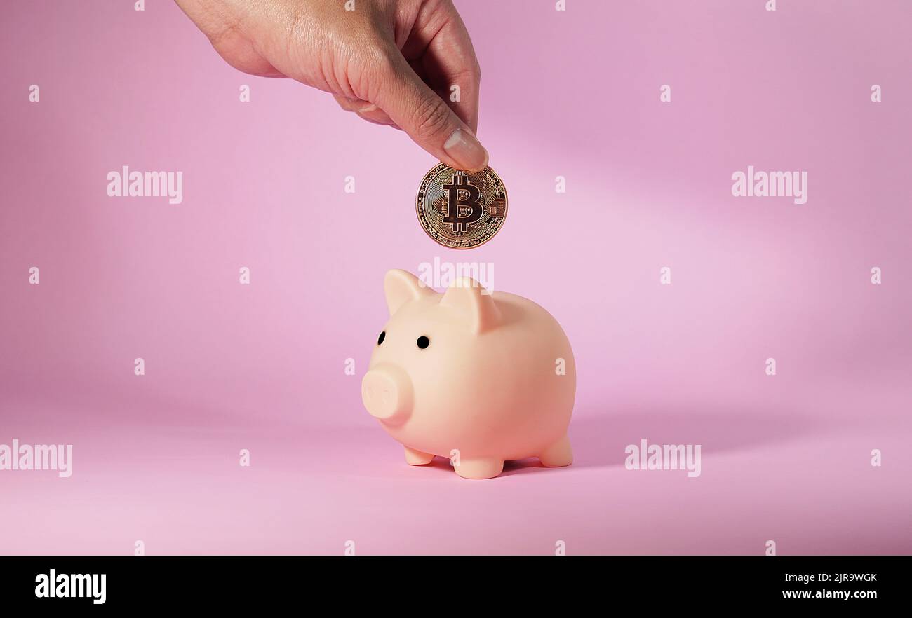 La main de l'homme dépose une pièce de monnaie en bitcoin métallique dans une banque de piggy. Affaires et finances. Banque D'Images