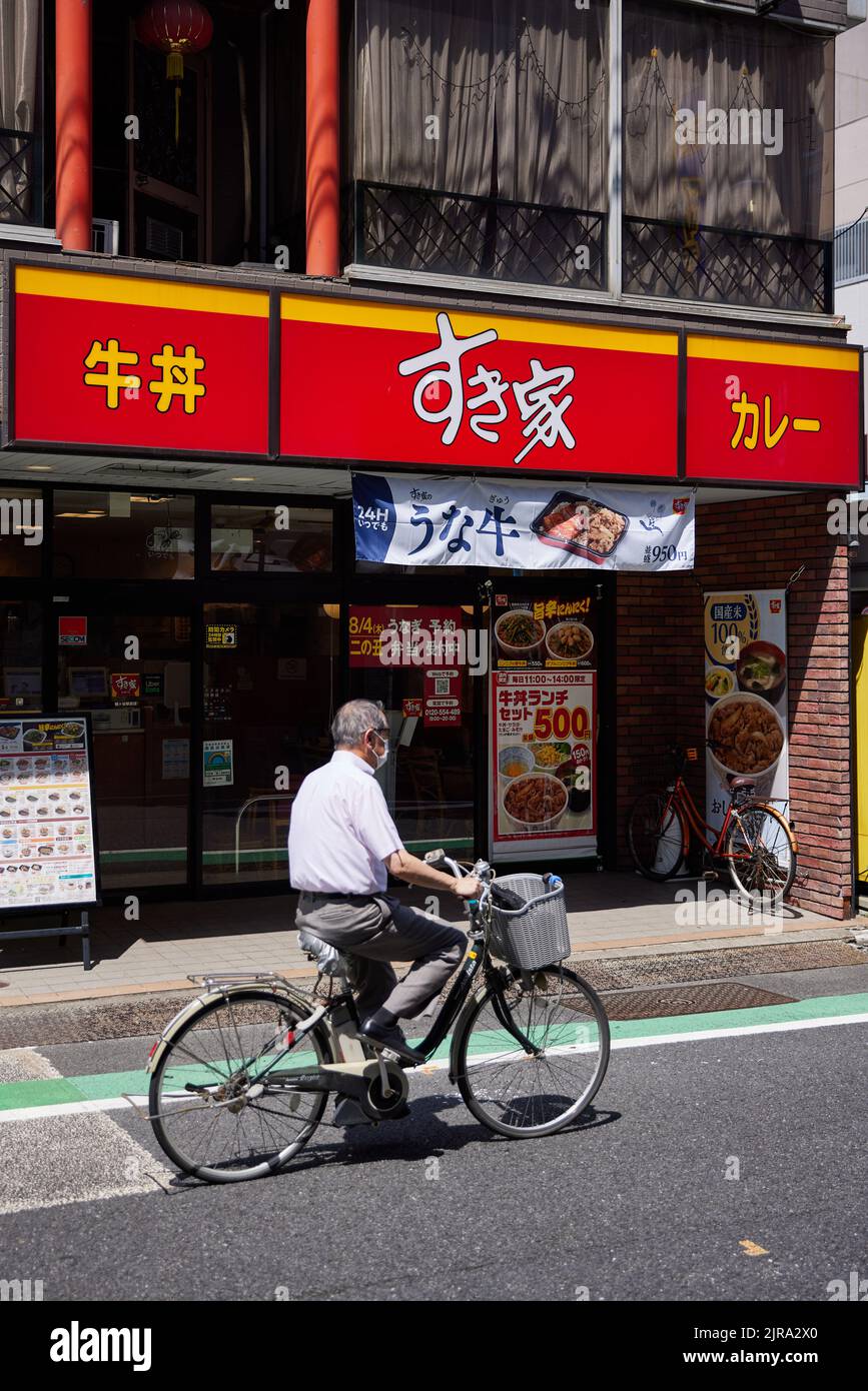 Sukiya (すき家), chaîne de restaurants gyudon (bol de boeuf), homme à vélo passant; Tokyo, Japon Banque D'Images