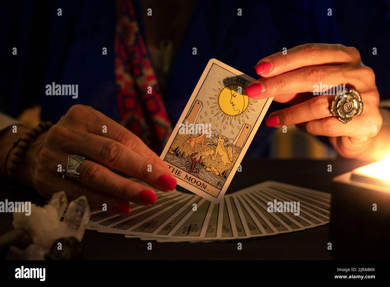 Les mains de la caissière montrant la carte de la Lune tarot, symbole de l'intuition, pendant une lecture. Gros plan avec bougie, ambiance feutrée. Banque D'Images