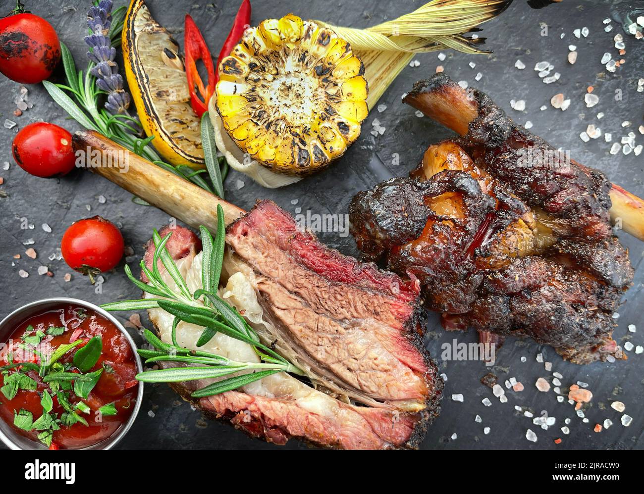 Côtes de bœuf grillées sur un tableau noir en ardoise avec maïs et sauce. Vue de dessus, gros plan Banque D'Images