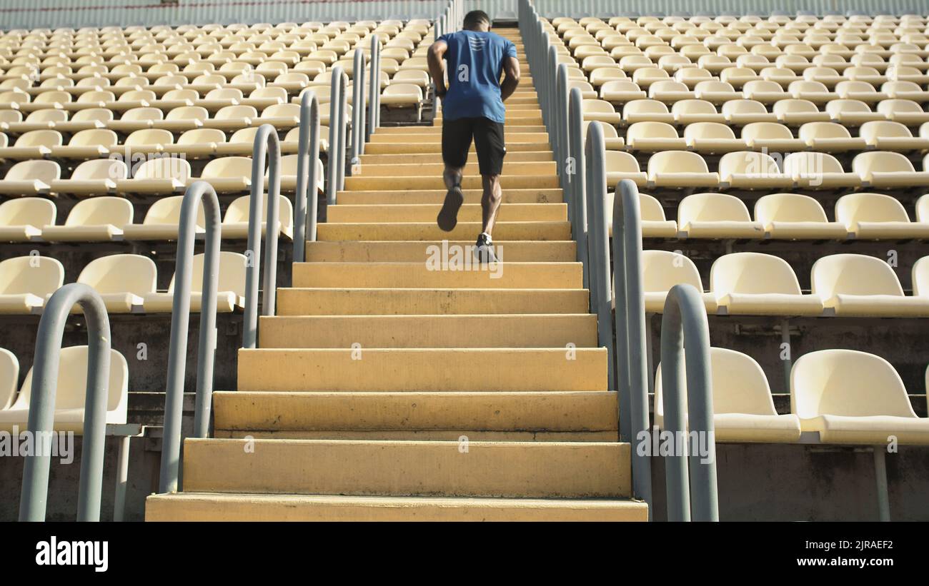 Vue arrière de l'athlète afro-américain qui court dans un escalier près des sièges pendant l'entraînement dans le stade Banque D'Images