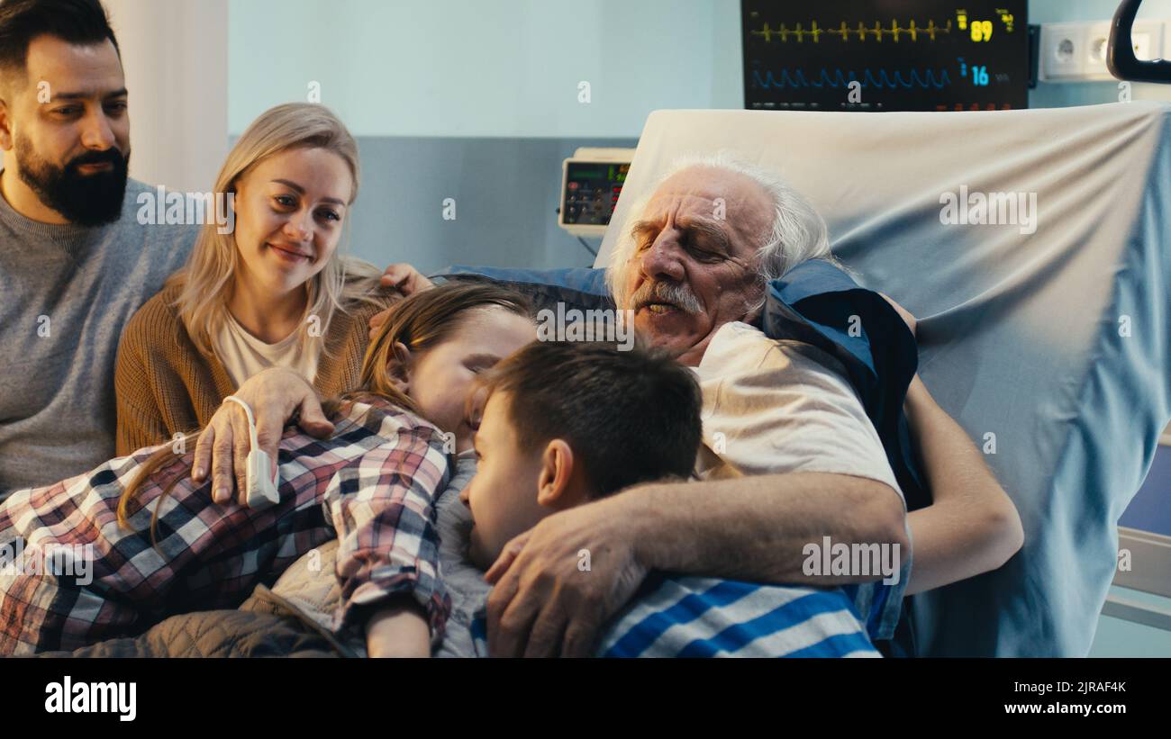 Un homme âgé embrasse des enfants et parle avec un homme et une femme adultes tout en étant allongé sur le lit dans le quartier de l'hôpital moderne Banque D'Images