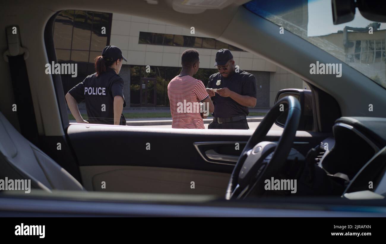 Homme afro-américain donnant un permis de conduire à des policiers multiraciaux puis retournant en voiture dans la rue de la ville Banque D'Images