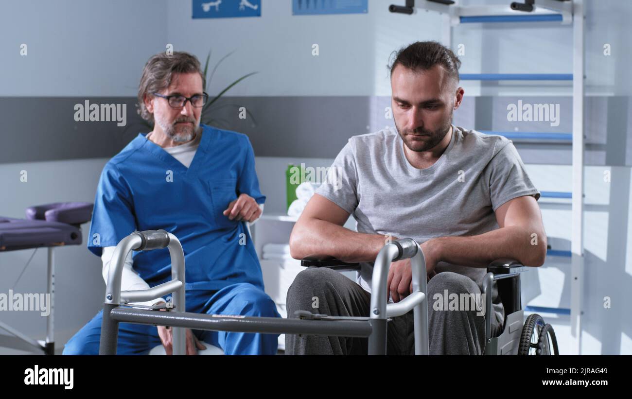 Thérapeute de réadaptation d'âge moyen parlant avec un homme déprimé en fauteuil roulant à l'hôpital Banque D'Images