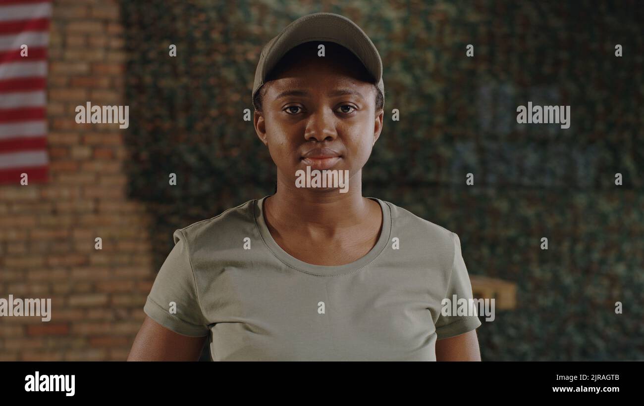 Femme noire soldat en t-shirt et casquette regardant la caméra avec un visage sérieux tout en se tenant contre le mur de brique sur la base militaire des États-Unis Banque D'Images