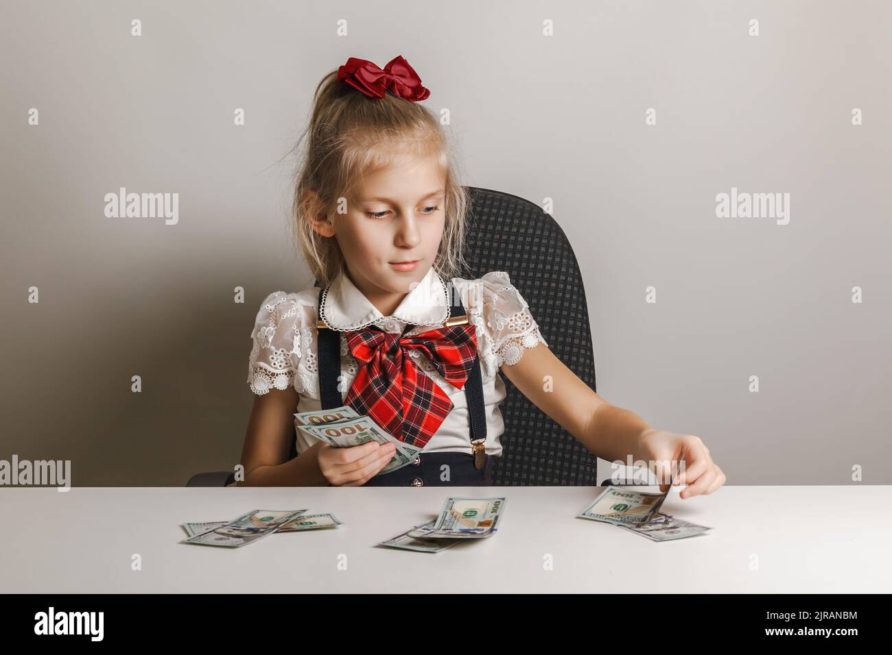 Une petite fille dans un uniforme d'école met l'argent dans des piles différentes. Enseigner aux enfants la littératie financière. Banque D'Images
