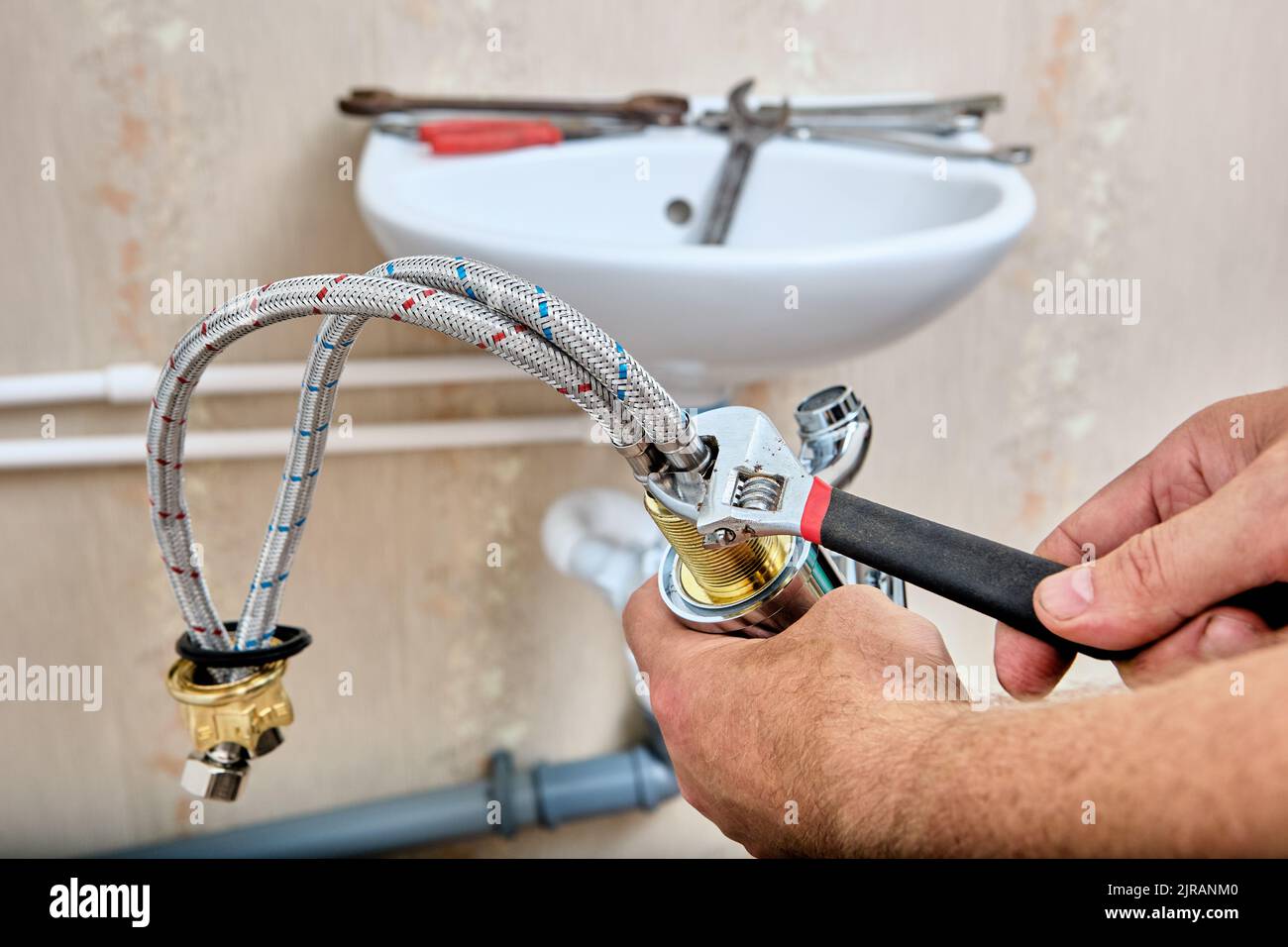 Le plombier fixe le tuyau de raccordement tressé au robinet d'eau avant d' installer le robinet sur l'évier de la salle de bains Photo Stock - Alamy