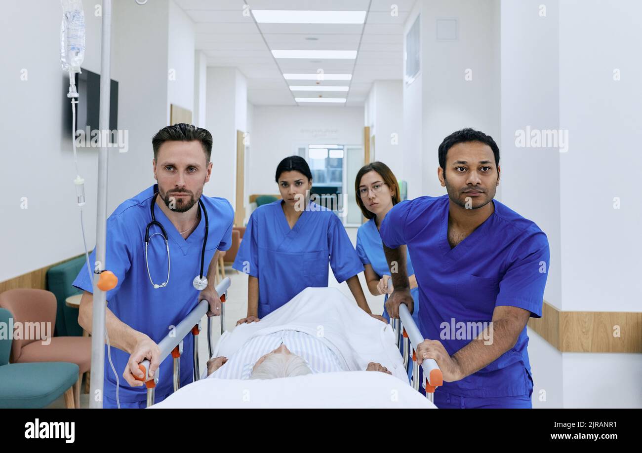 médecins et infirmières qui roulent un patient âgé en brancard dans le couloir hospitalier aux urgences. Le travail de l'équipe médicale d'urgence et des paramédicaux Banque D'Images
