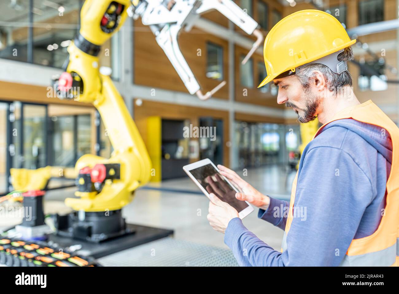 Un travailleur qualifié contrôlant le bras du robot avec une tablette numérique Banque D'Images