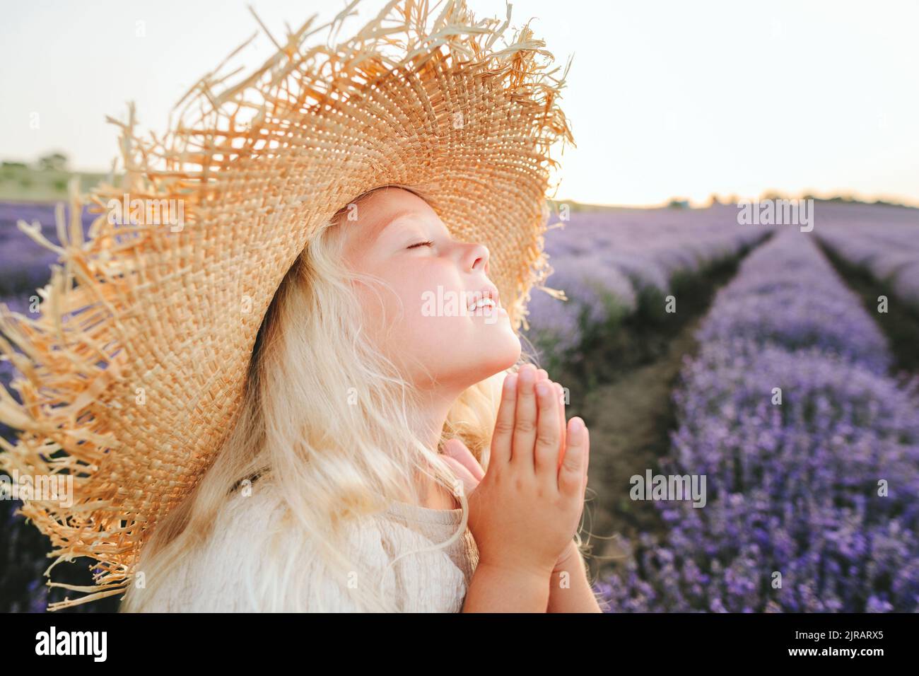 Fille souriante avec les yeux fermés priant dans le champ de lavande Banque D'Images
