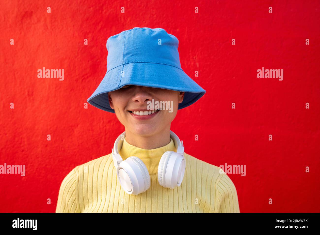 Femme souriante avec casque et chapeau seau bleu devant le mur rouge Banque D'Images