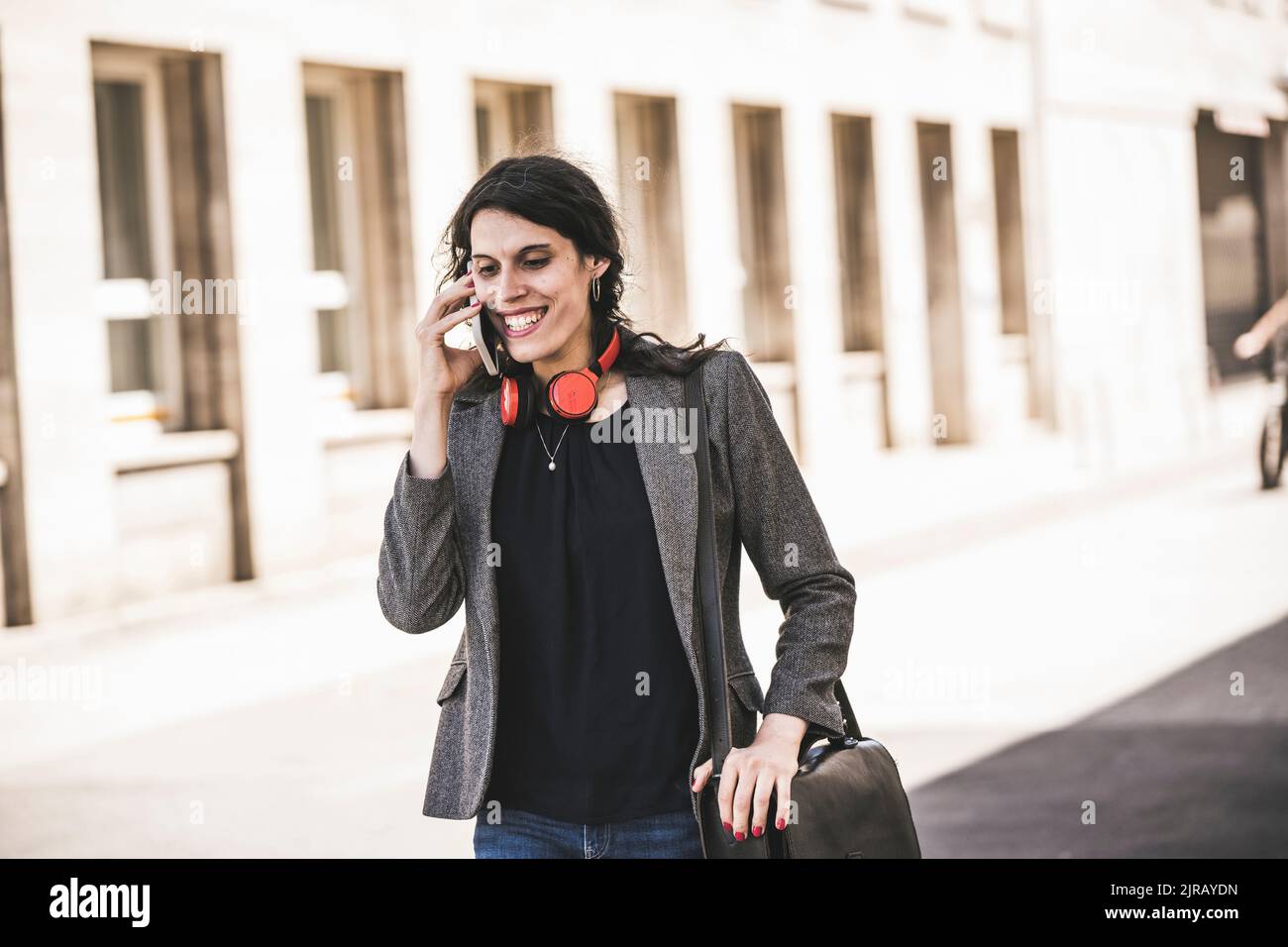Femme d'affaires souriante et transgenre portant un blazer parlant au téléphone Banque D'Images