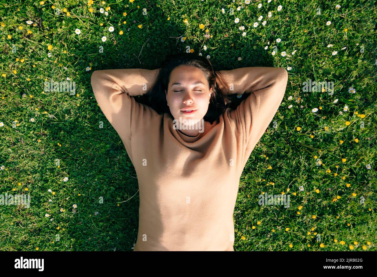 Jeune femme avec les mains derrière la tête allongé sur l'herbe au parc Banque D'Images