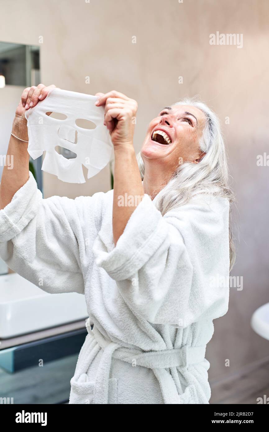 Femme mûre avec masque facial riant dans la salle de bains à la maison Banque D'Images