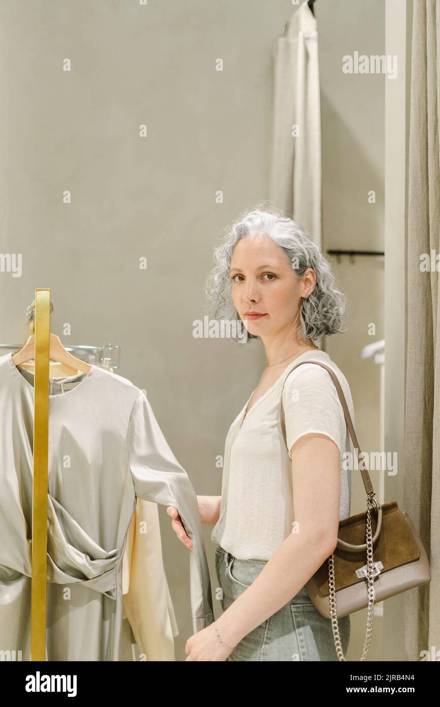 Femme avec sac en toile debout près du porte-vêtements au magasin Banque D'Images