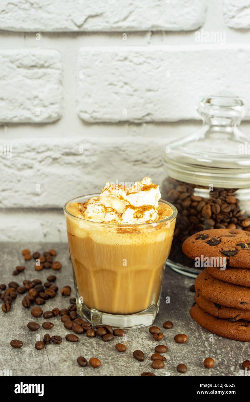 Café latte au caramel dans un verre avec crème fouettée et biscuit au chocolat. Grains de café sur une surface murale en brique grise et blanche avec espace de copie. Banque D'Images