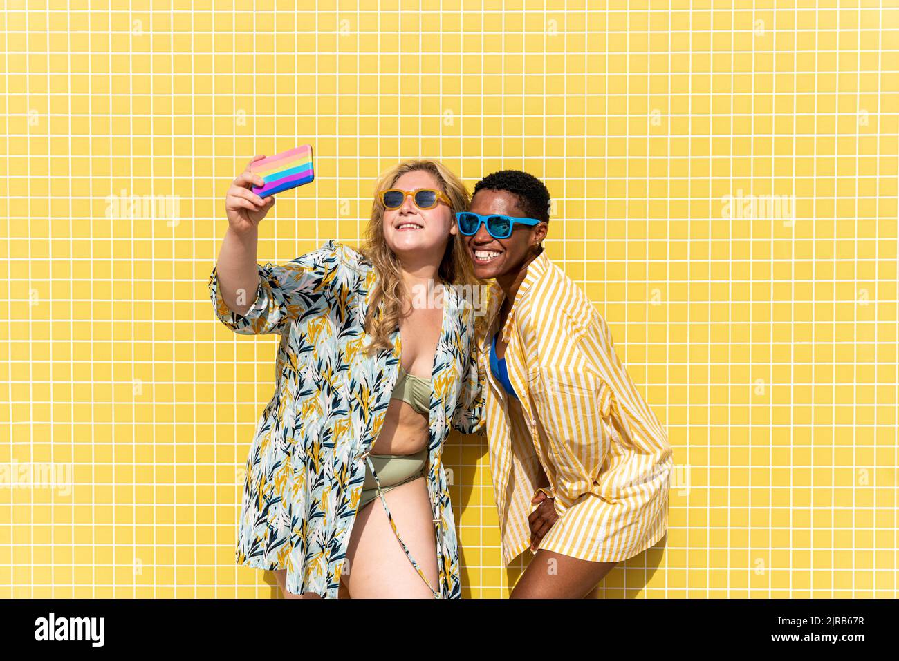 Bonne femme prenant selfie avec un ami devant le mur jaune Banque D'Images