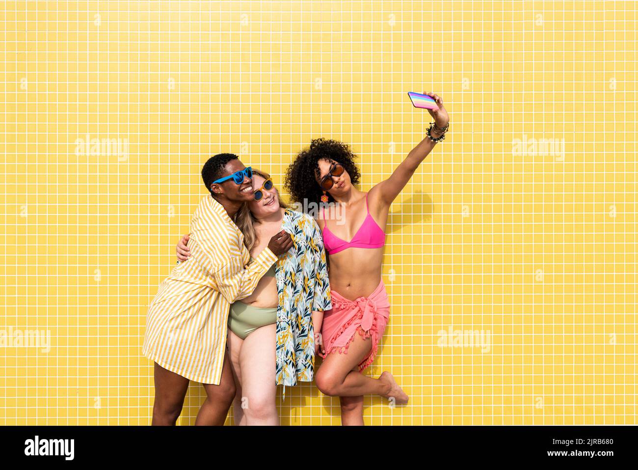 Les femmes multiraciales prennent le selfie par téléphone portable devant le mur jaune Banque D'Images