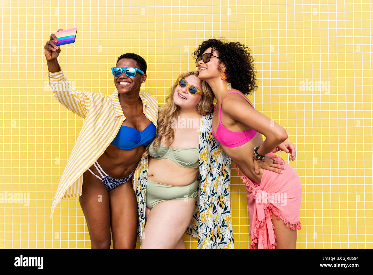 Des amis joyeux qui prennent le selfie à travers un smartphone dans un mur jaune Banque D'Images