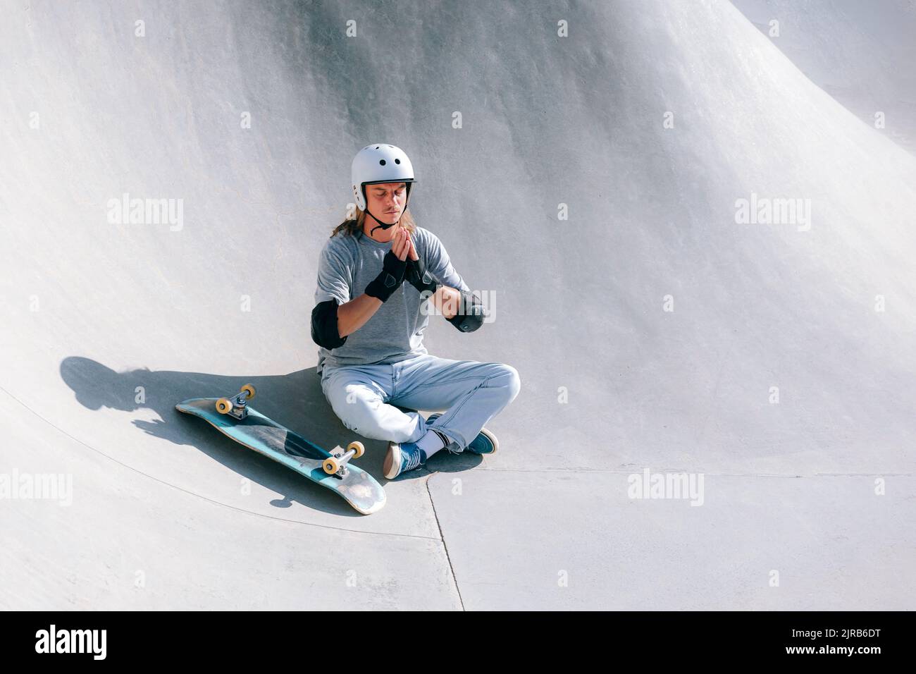 Skateboarder faisant du yoga avec les mains jointes dans le parc de skate Banque D'Images