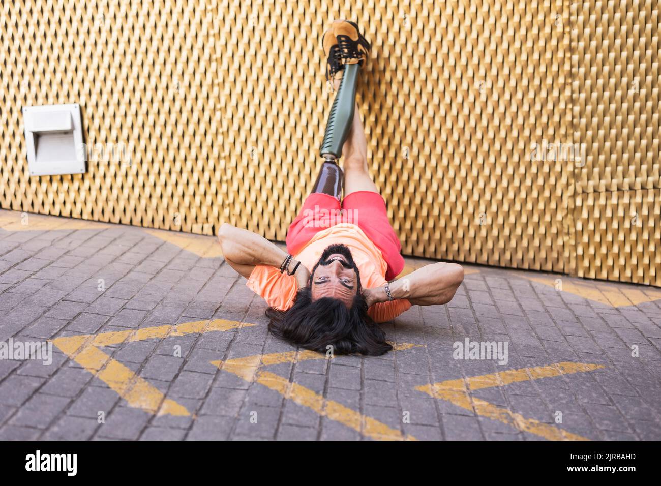 Homme barbu souriant avec une jambe prothétique couché sur la route Banque D'Images