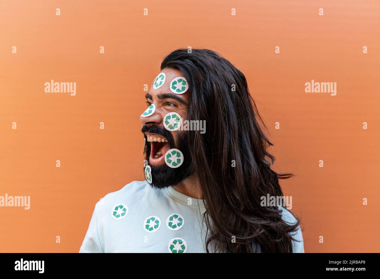Crier un homme barbu avec des autocollants de recyclage sur le visage devant le mur Banque D'Images