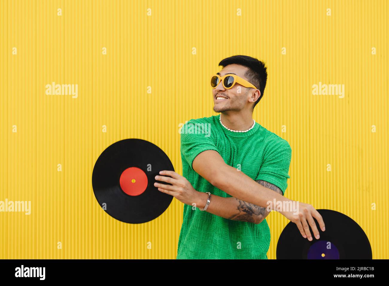 Joyeux jeune homme s'amusant avec des disques en vinyle devant le mur Banque D'Images