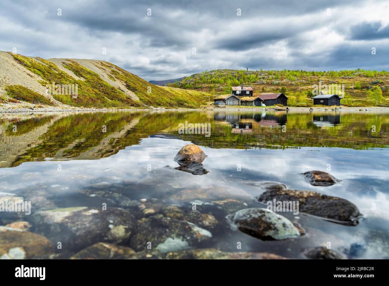 Norvège, Innlandet, bord de lac des Rocheuses dans le parc national de Jotunheimen avec des huttes isolées en arrière-plan Banque D'Images