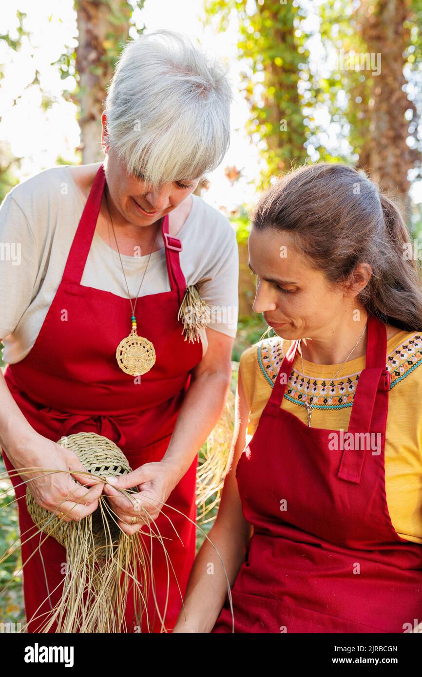 Un artisan souriant montrant la fabrication d'un panier avec de l'herbe esparto à un collègue Banque D'Images