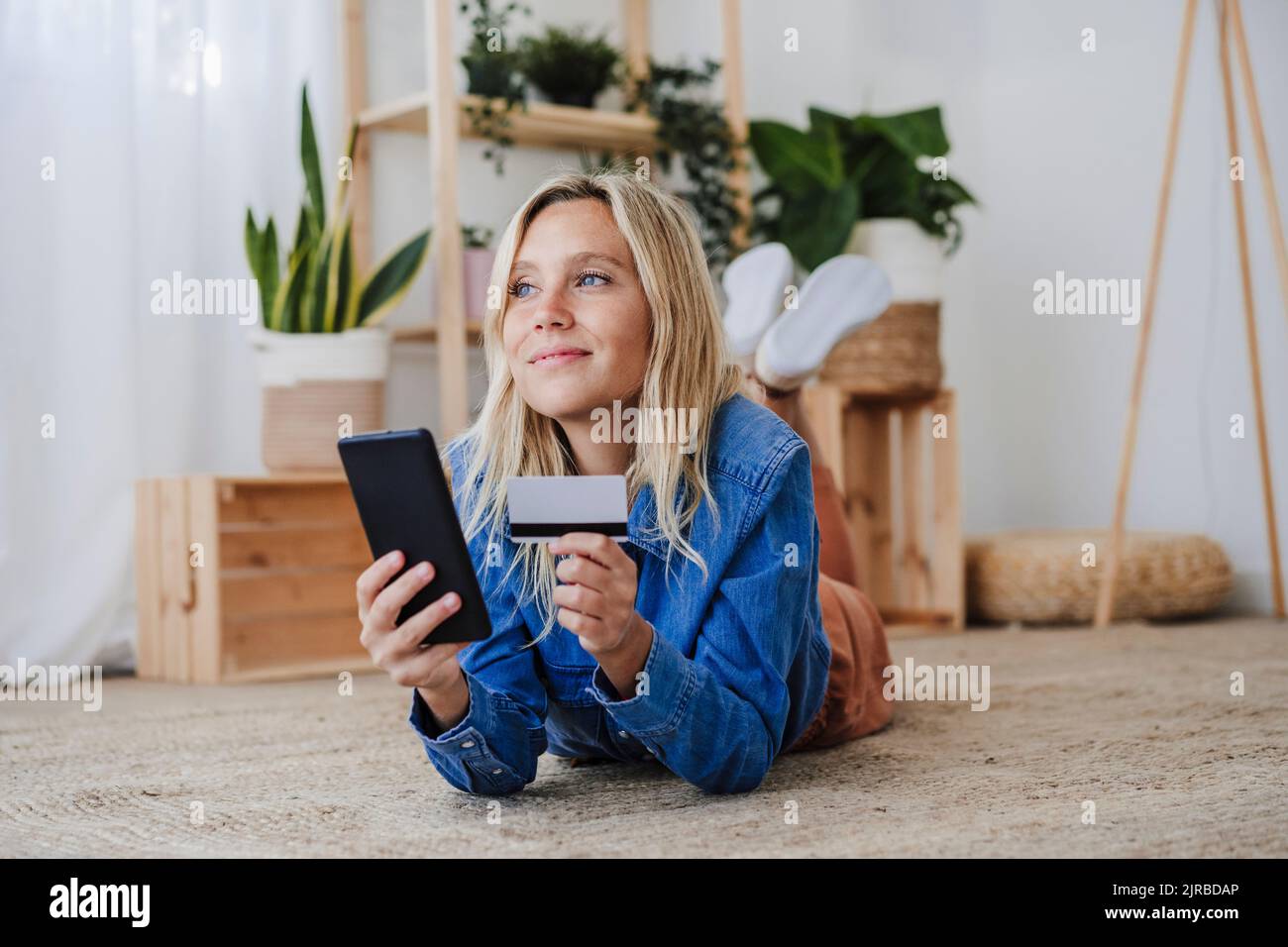 Femme contemplative faisant des achats en ligne sur le sol à la maison Banque D'Images