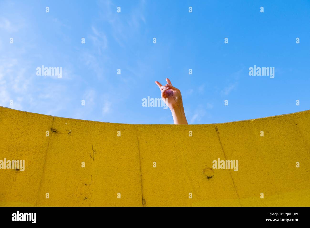 Main de la jeune femme montrant le geste de paix devant le ciel bleu Banque D'Images