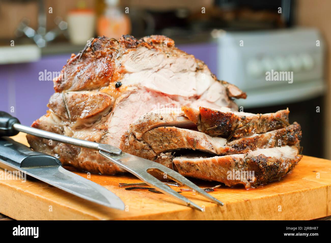 Viande de porc cuite avec épices tranchées sur une planche à découper brune avec couteau et fourchette. Banque D'Images